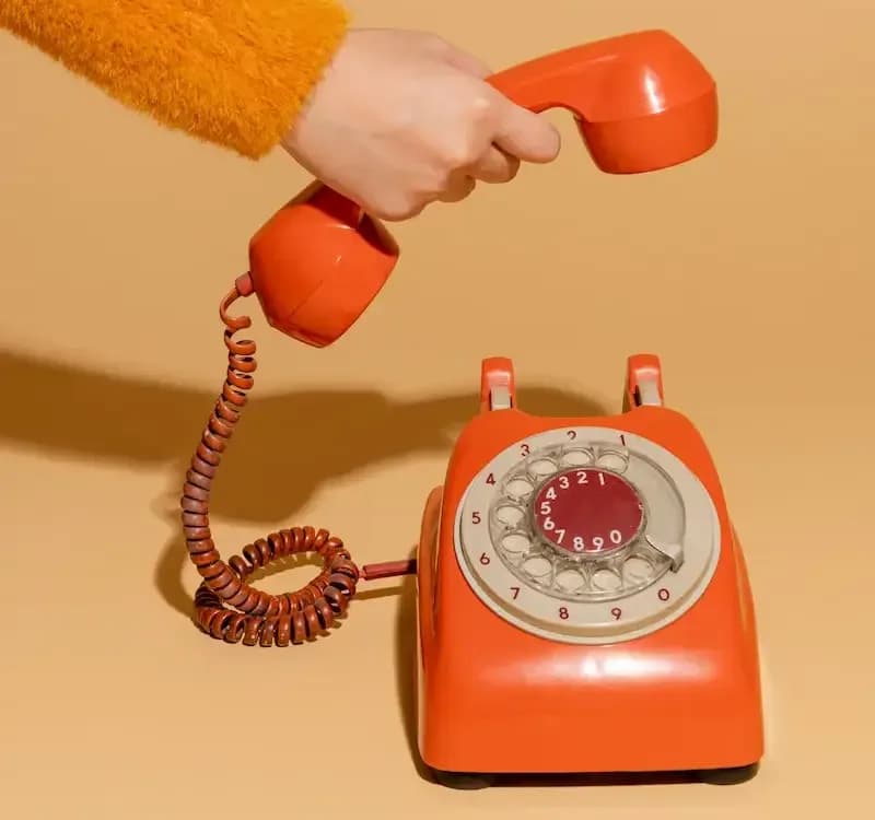 Une main qui décroche un téléphone rétro orange